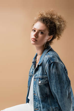 Curly model in denim jacket looking at camera isolated on beigeの写真素材