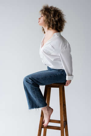 Side view of stylish barefoot model sitting on chair isolated on whiteの写真素材