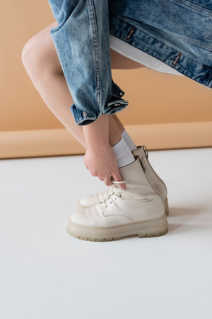 Cropped view of young woman touching stylish boots on beige backgroundの写真素材