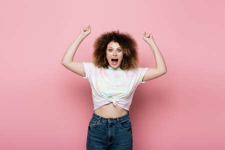 Excited woman in jeans and t-shirt showing yes gesture showing on pink background