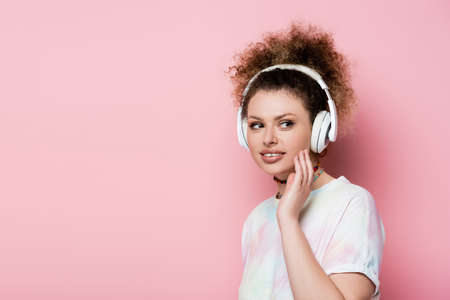 Smiling woman in headphones looking away isolated on pinkの写真素材