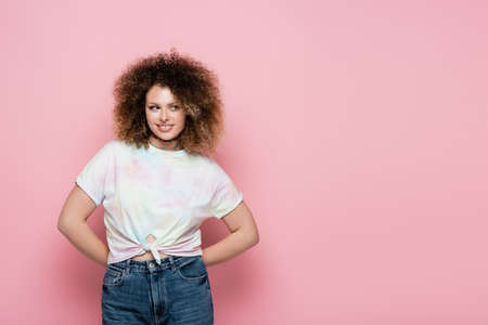 Smiling curly woman in t-shirt looking away on pink backgroundの写真素材