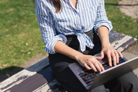 cropped view of woman typing on laptop keyboard while sitting on benchの写真素材
