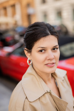 portrait of brunette woman in beige and trendy coat looking awayの写真素材