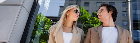low angle view of young man and blonde woman in sunglasses looking at each other outdoors, bannerの写真素材