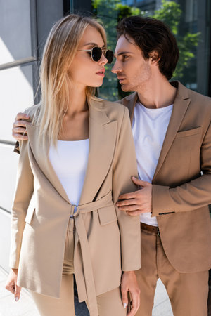 brunette man embracing stylish woman in sunglasses on urban streetの写真素材