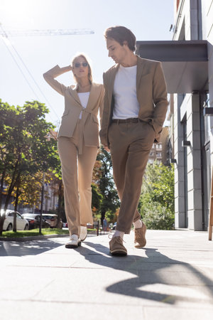 full length view of young couple in beige suits walking in cityの写真素材