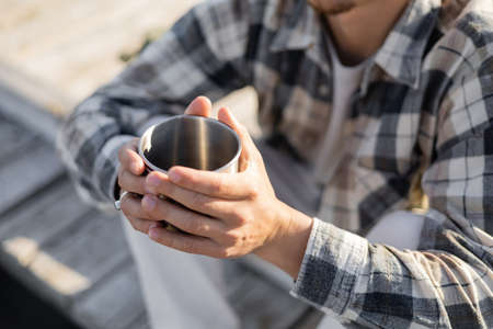 Cropped view of blurred man holding cup on wooden pierの写真素材