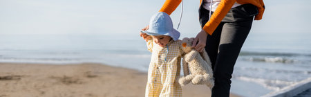 Woman holding toddler kid and toy on beach in Treviso, bannerの写真素材