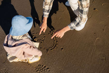 High angle view of man drawing heart sign on sand near toddler daughterの写真素材