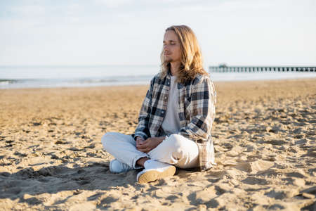 Young long haired man meditating on beach in Italyの写真素材