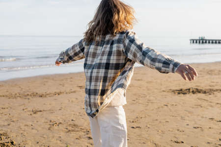 Back view of long haired man in checkered shirt walking on beach in Trevisoの写真素材