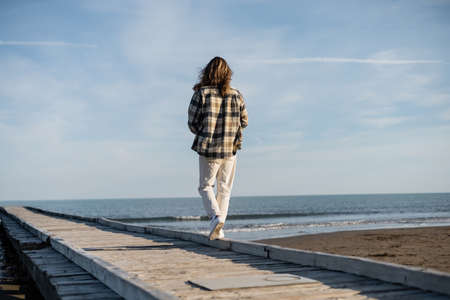 Back view of long haired man walking on wooden pier near adriatic sea in Italy