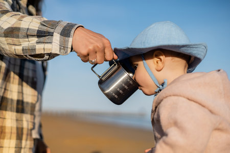 Father holding cup near baby in panama hat on beachの写真素材
