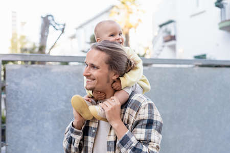 Smiling baby sitting on shoulders of young father on urban street in Trevisoの写真素材