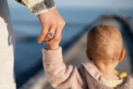 Back view of father holding hand of blurred toddler daughter on pierの写真素材