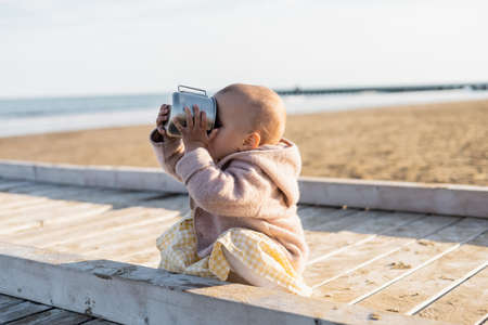 Baby girl drinking from cup on beach in Italyの写真素材