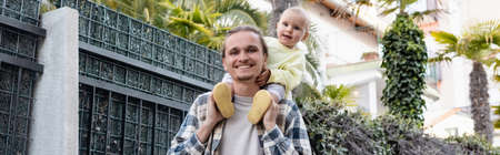 Young man holding baby on shoulders and smiling at camera on urban street in Treviso, bannerの写真素材
