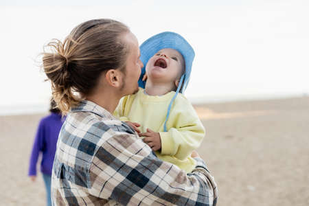 Father holding laughing toddler child in panama hat on beachの写真素材