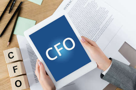 cropped view of woman holding digital tablet with cfo letters on screen near wooden cubes and documentsの写真素材