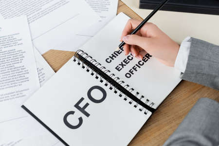cropped view of woman holding pencil near notebook with cfo and chief executive officer letteringの写真素材
