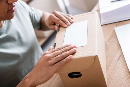 Cropped view of african american seller applying shipping label on carton box in shopの写真素材