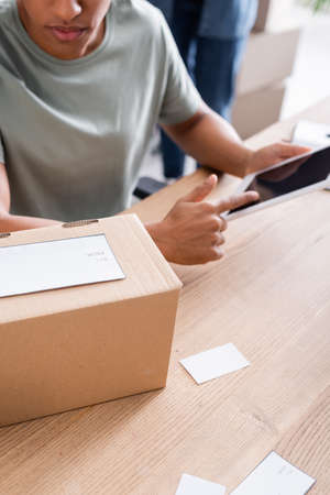 Cropped view of african american seller using digital tablet near cardboard box in online web storeの写真素材