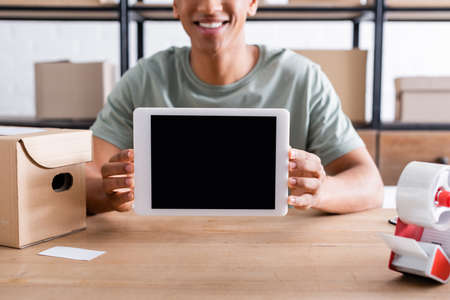 Cropped view of smiling african american seller holding digital tablet near adhesive tape and cardboard boxの写真素材