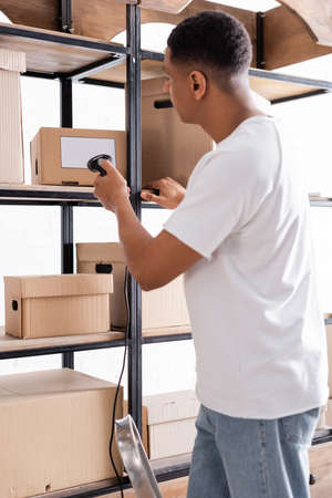 Side view of african american online web store owner scanning packages on rackの写真素材
