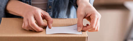 Cropped view of online web store owner fastening shipping label on carton box, bannerの写真素材