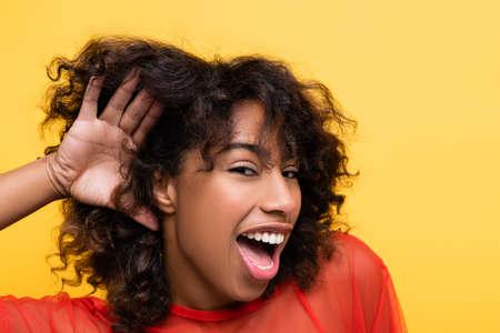 astonished african american woman showing cant hear gesture isolated on yellowの写真素材