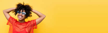 joyful african american woman in red top and blue sunglasses posing isolated on yellow, banner