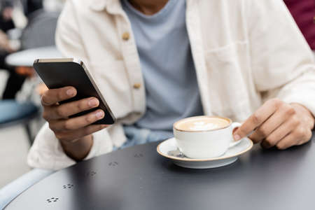 partial view of african american man texting on smartphone near cappuccino on tableの写真素材