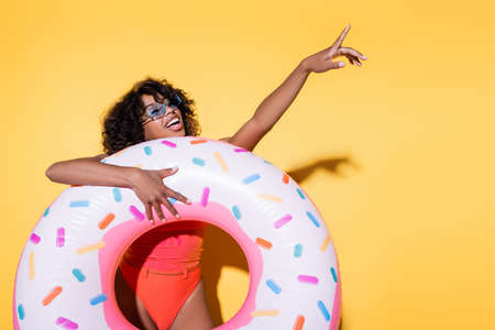 happy african american woman holding swim ring and pointing with finger on yellow backgroundの写真素材