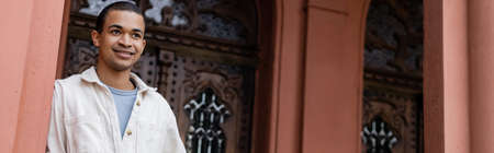 happy african american man in shirt jacket posing near building in europe, bannerの写真素材