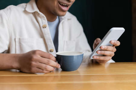 cropped view of cheerful african american man texting on smartphone near cup on tableの写真素材