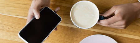top view of african american man holding smartphone and cup of cappuccino, banner