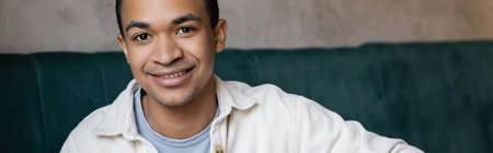 positive and young african american man looking at camera in coffee shop, bannerの写真素材