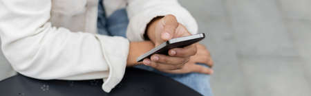 partial view of african american man texting on smartphone outside, banner