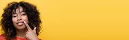 brunette african american woman pointing with finger at her smile isolated on yellow, banner