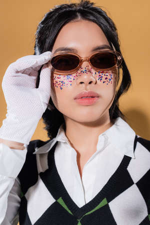 Portrait of stylish asian model holding sunglasses on orange background