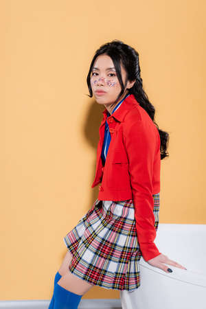 Trendy asian model looking at camera near bathtub on orange backgroundの写真素材