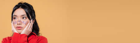 Asian model with glitter on face looking away isolated on orange, banner