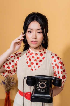 Asian model holding vintage telephone and looking at camera on orange backgroundの写真素材