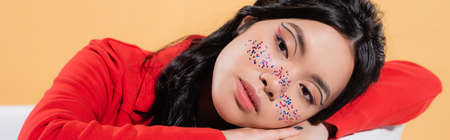 Stylish asian model with glitter makeup sitting in bathtub isolated on orange, bannerの写真素材