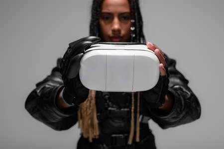 Vr headset in hands of blurred african american woman isolated on greyの写真素材