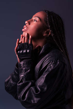 Side view of stylish african american woman in leather jacket and glove looking away isolated on dark greyの写真素材