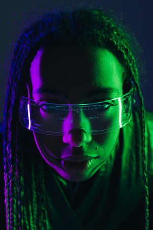 Portrait of african american woman with pigtails using smart glasses isolated on dark blue