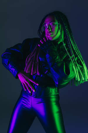 Stylish african american woman in leather jacket and smart glasses looking at camera isolated on dark blueの写真素材