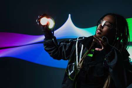African american woman in smart glasses holding lights on grey background with abstraction